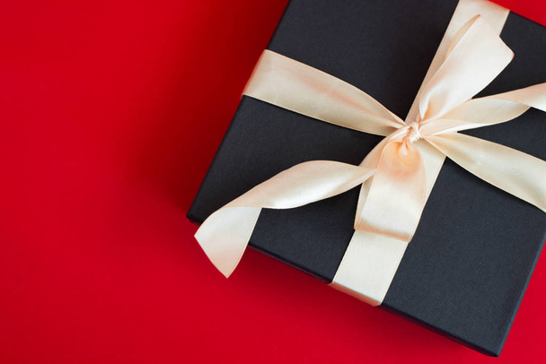 black gift box with gold ribbon and a bow on red background - Fotoğraf, Görsel