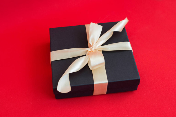 black gift box with gold ribbon and a bow on red background - Foto, immagini