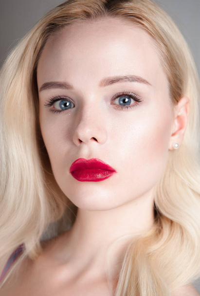 Beauty model girl with perfect make-up red lips and blue eyes looking at camera. Portrait of attractive young woman with blond hair. Beautiful female face with clear fresh skin. Fashion close up shot. - 写真・画像