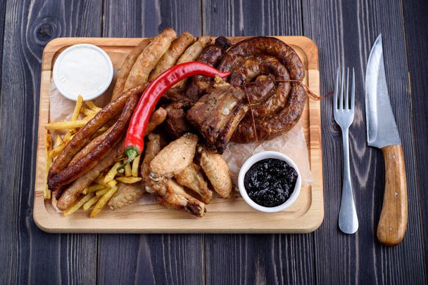 Grilled sausages and chicken with fries on a wooden board - Fotoğraf, Görsel