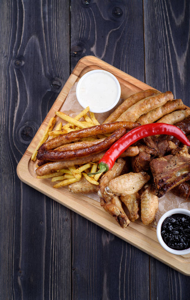 Grilled sausages and chicken with fries on a wooden board - Fotografie, Obrázek