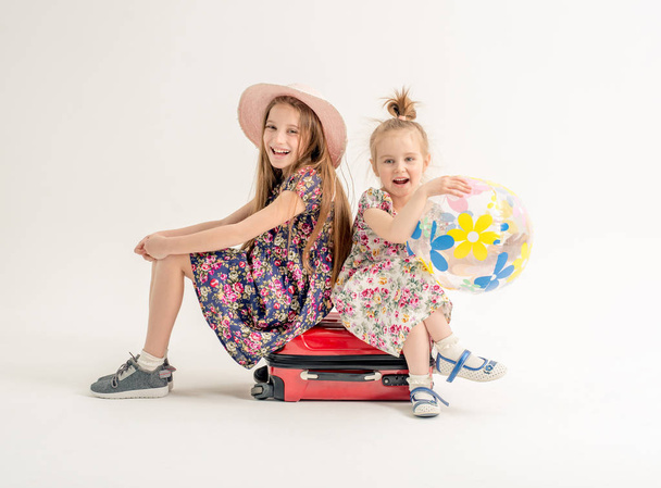 Happy sisters are sitting on a suitcase - Foto, afbeelding