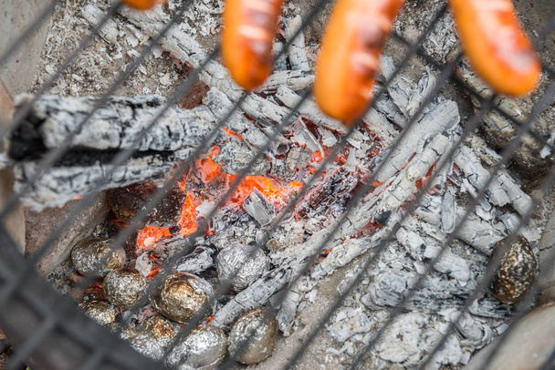 Grillrost mit Würstchen an einem alten Feuertopf mit Bratkartoffeln - Foto, Bild