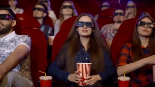 Vrienden in de bioscoop kijken naar een boeiende film in 3d bril, cola drinken en eten popcorn. - Video