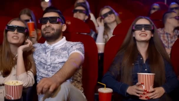 Friends at the cinema watching a fascinating film in 3D glasses, drinking cola and eating popcorn. - Footage, Video