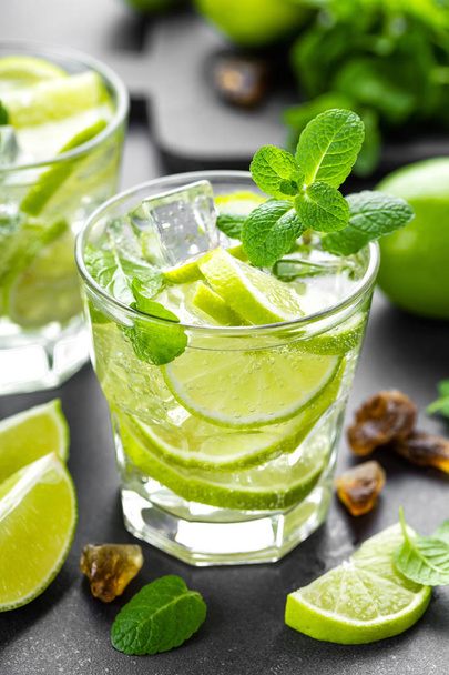Summer mint lime refreshing cocktail mojito with rum and ice in glass on black background top view - 写真・画像