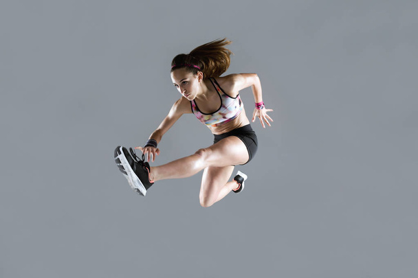 Fit and sporty young woman jumping on white background. - Фото, изображение