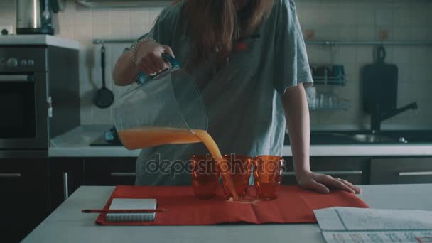 Träges brünettes Mädchen gießt Orangensaft in rotes Glas und verschüttet es überall - Filmmaterial, Video