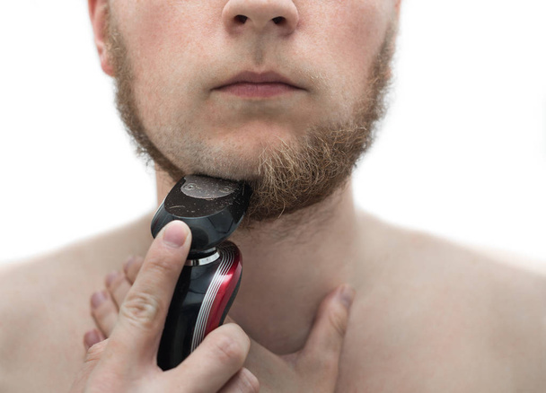 Nuori mies ajelee partansa parranajokoneella.
 - Valokuva, kuva