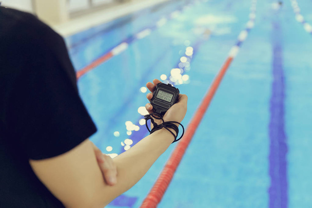 χέρι του προπονητή με ένα χρονόμετρο με διακόπτη κατά τη διάρκεια αγώνων στην πισίνα. - Φωτογραφία, εικόνα
