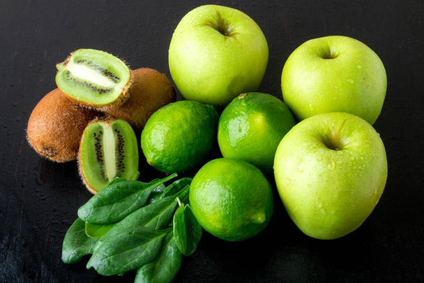 スムージーの材料。黒の木製の背景に緑の果実。リンゴ、ライム、ほうれん草、キウイ。デトックス。健康食品. - 写真・画像