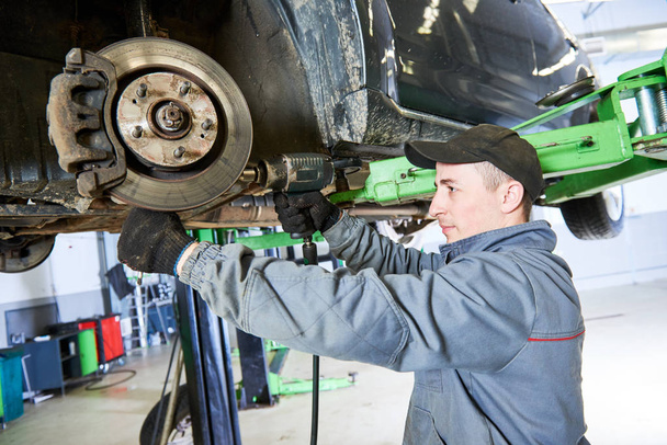 Auto repair service. Mechanic works with car suspension - Foto, afbeelding