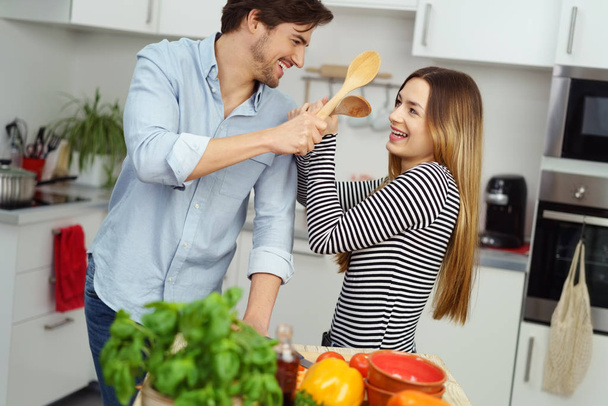 Laughing young couple mock fighting in the kitchen - Фото, зображення