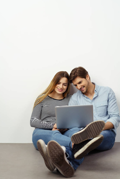 Young couple relaxing on the floor with a laptop - Photo, image