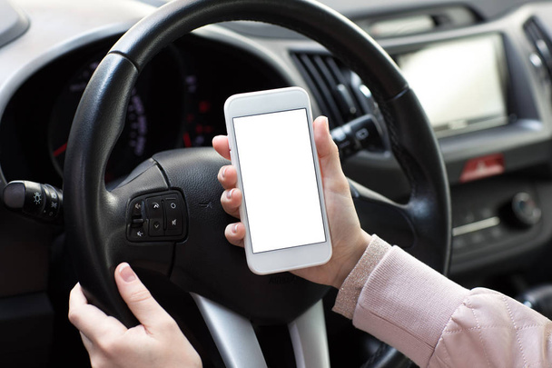 Female hands holding phone with isolated screen behind wheel car - Fotó, kép