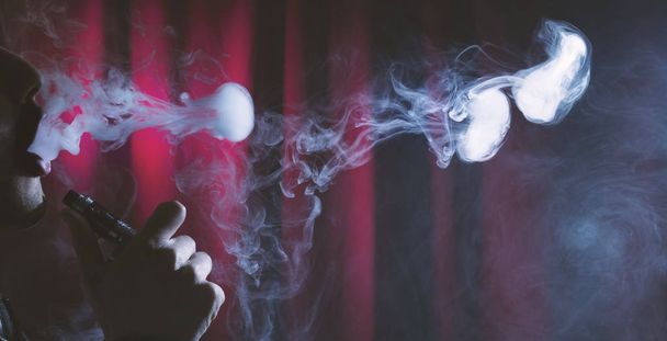young man vaping clouds on a dark background. - Photo, Image