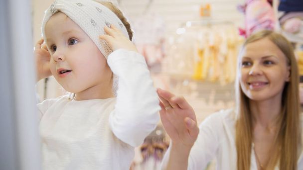 Kézműves ruha bolt - kis szőke kislány, anya csinál vásárlás és vásárlási szép kalap - Fotó, kép