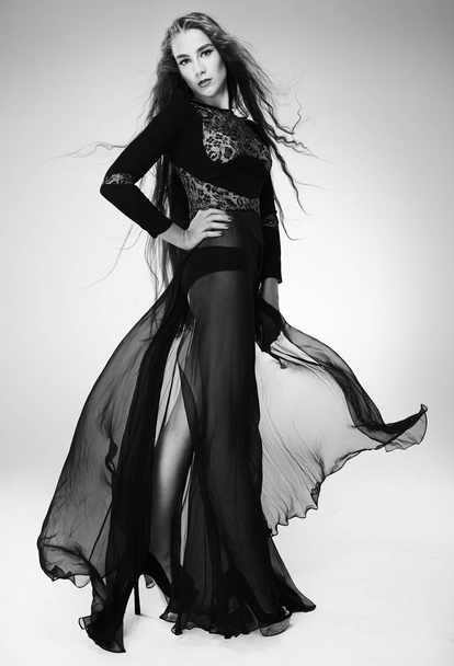 schöne Frau mit erstaunlich langen Haaren in langen luftigen schwarzen Kleid posiert im Studio - Foto, Bild