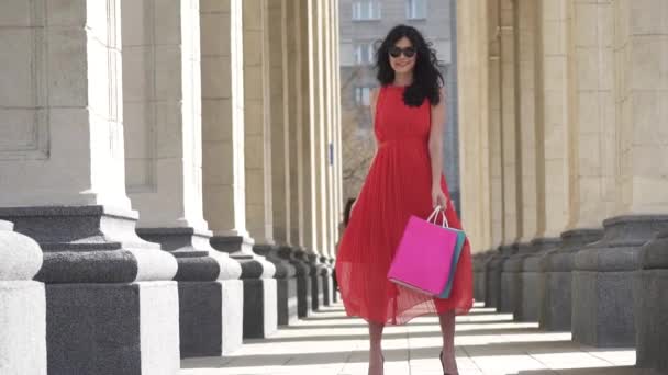 Charming girl with shopping bags in hands.. The brunette is happy with successful shopping, she smiles and rejoices. Charming girl with shopping bags in hands. Professional model posing on camera. - Footage, Video