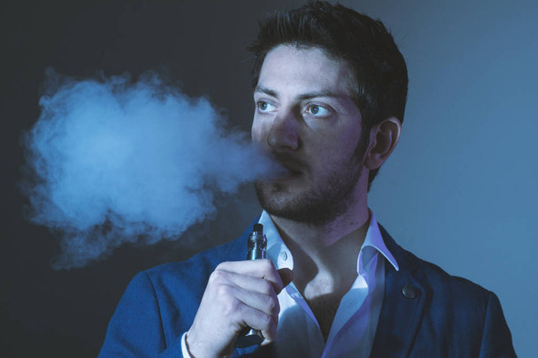 Απομονωμένη νεαρός άνδρας σε ένα σκοτεινό φόντο κρατώντας ένα ηλεκτρονικό τσιγάρο - Φωτογραφία, εικόνα