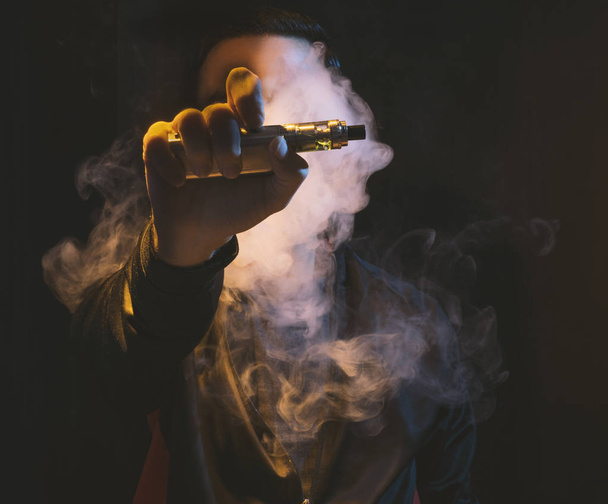 geïsoleerde man vaping e sigaret op een donkere achtergrond - Foto, afbeelding
