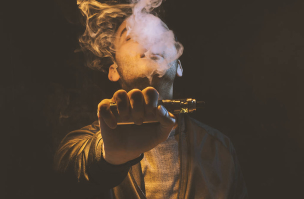 isolated man vaping e cigarette over a dark background - Photo, image