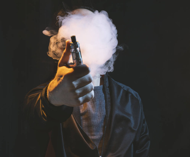 isolated man vaping e cigarette over a dark background - Photo, Image