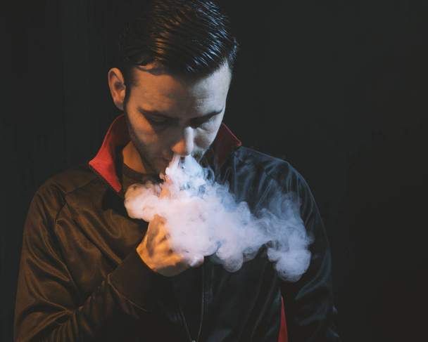 mężczyzna na białym tle vaping e papieros na ciemnym tle - Zdjęcie, obraz