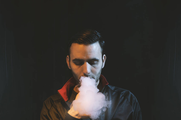 isolated man vaping e cigarette over a dark background - Фото, изображение