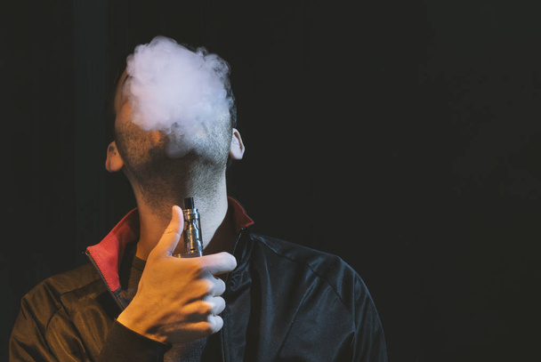 isolated man vaping e cigarette over a dark background - Fotoğraf, Görsel