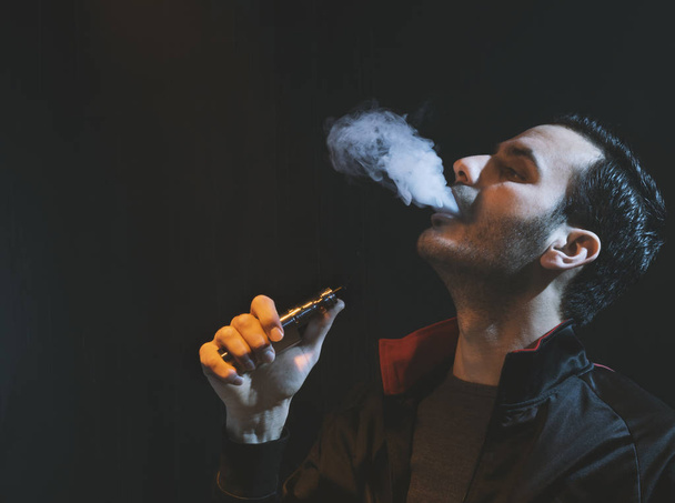 isolierter Mann verdampft E-Zigarette vor dunklem Hintergrund - Foto, Bild