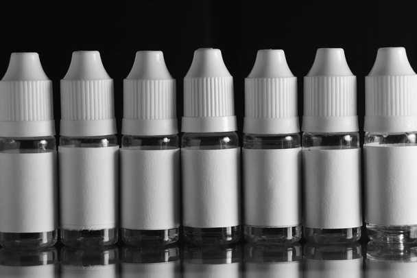 Vereinzelte E-Zigaretten- und Flüssigkeitsflaschen vor schwarzem Hintergrund. - Foto, Bild