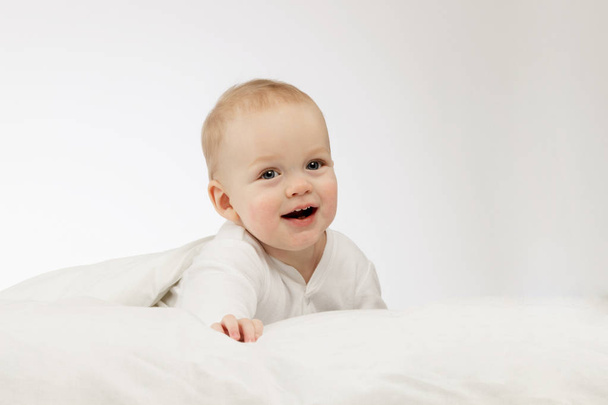 Smilling ładny chłopiec 9 miesiąca w bodysuite biały na białym tle. Śmiejąc się niemowlę noworodek pod koc. Miejsce. - Zdjęcie, obraz