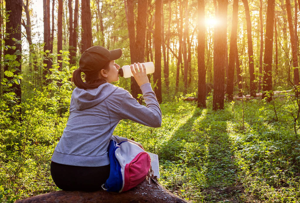 Дівчина з рюкзаком п'є воду в лісі
 - Фото, зображення