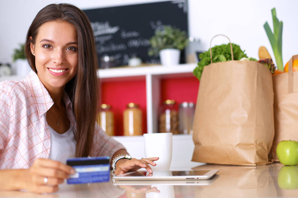 Smiling woman online shopping using tablet and credit card in kitchen - Foto, immagini