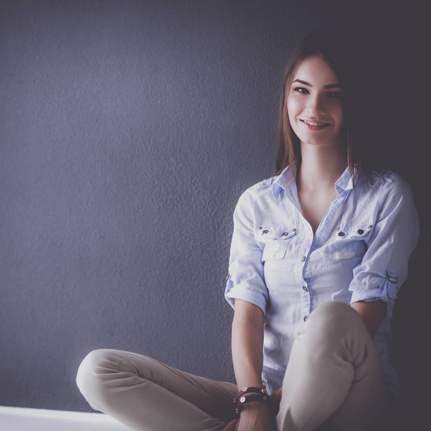 Jovem mulher sentada no chão perto da parede escura - Foto, Imagem