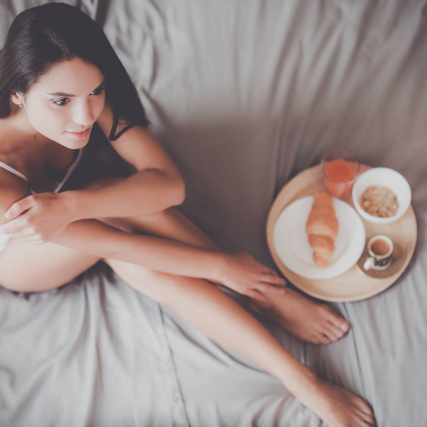 Young woman sitting in bed with a cup of milk - 写真・画像