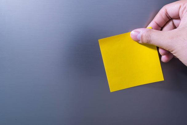 Γκρο πλαν του ατόμου χέρι που κρατά κενή σημείωση κίτρινο Sticked στην πόρτα του ψυγείου - Φωτογραφία, εικόνα