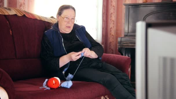 Old lady at home - senior woman watching TV and knits wool socks - Footage, Video
