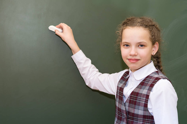 girl in a school uniform is standing in front of a green board - Фото, зображення