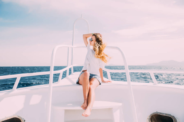 Vrolijke jonge vrouw leunt op de leuning en glimlachend in de camera terwijl staande op de boeg van het schip - Foto, afbeelding