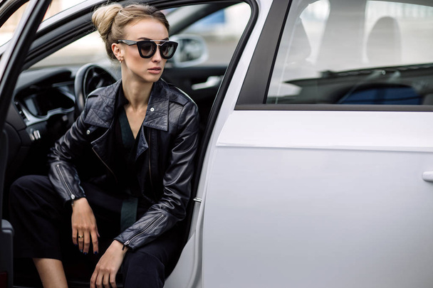fashion outdoor photo of sexy beautiful woman with dark hair in black leather jacket and sunglasses posing in luxurious auto - Φωτογραφία, εικόνα