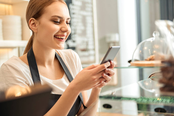 Happy female worker messaging on smartphone in cafe - Photo, Image