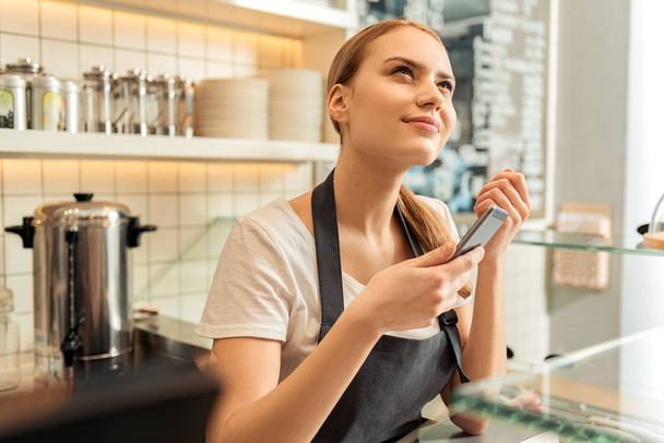 Thoughtful waitress using phone in cafe - Zdjęcie, obraz