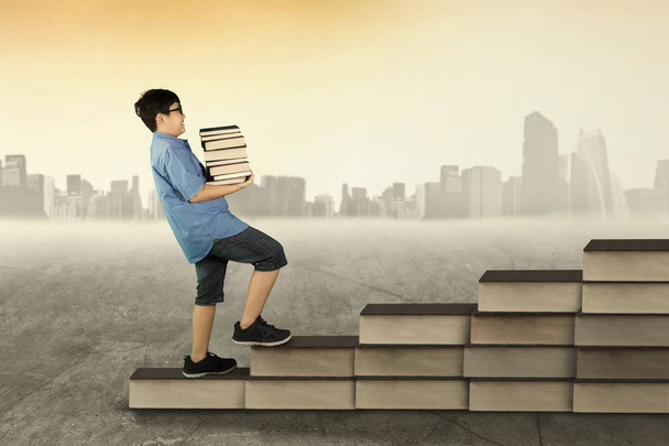 Boy holds books and walk on books stair - Photo, image