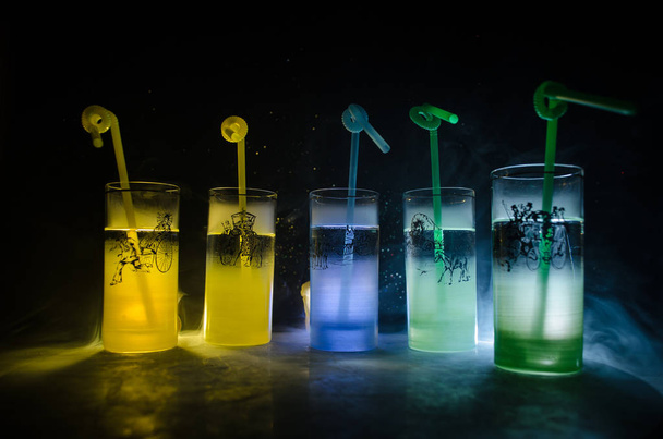 Five cocktails on the bar with smoke on dark background. Yellow, green and blue colored glasses. - Photo, Image