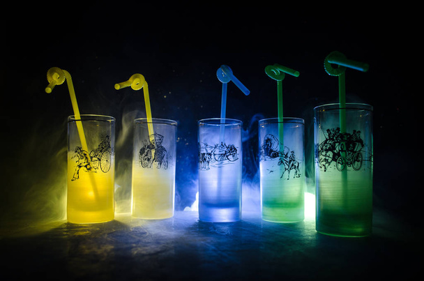 Fünf Cocktails an der Bar mit Rauch auf dunklem Hintergrund. gelbe, grüne und blaue Gläser. - Foto, Bild