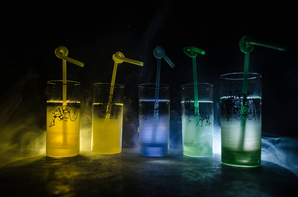 Fünf Cocktails an der Bar mit Rauch auf dunklem Hintergrund. gelbe, grüne und blaue Gläser. - Foto, Bild