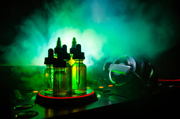 Vape and DJ Club concept. Smoke clouds and vape liquid bottles on Dj mixer close up. Light effects. Useful as background or vape or club advertisement or vape background. - Photo, Image