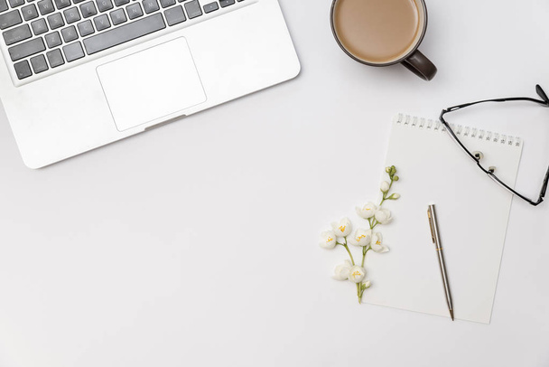 werkplek met lege notebook, tak van bloem jasmijn, kopje koffie en laptop - Foto, afbeelding